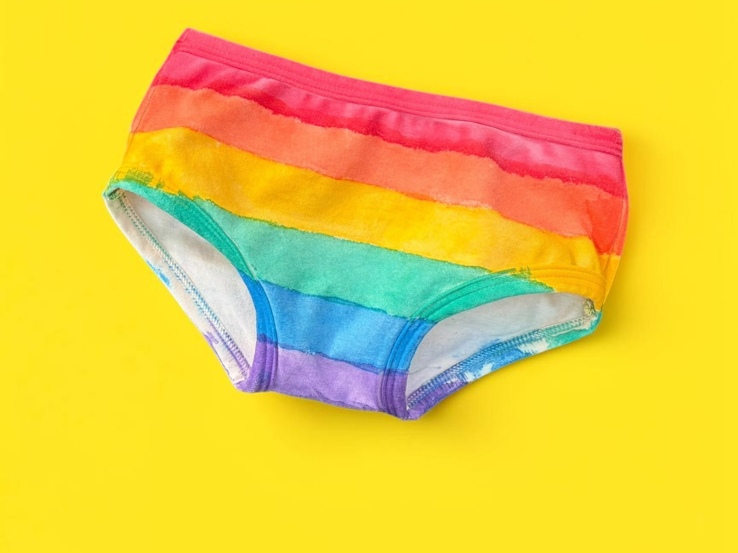 Rainbow-striped kids briefs laid flat on a bright yellow background.