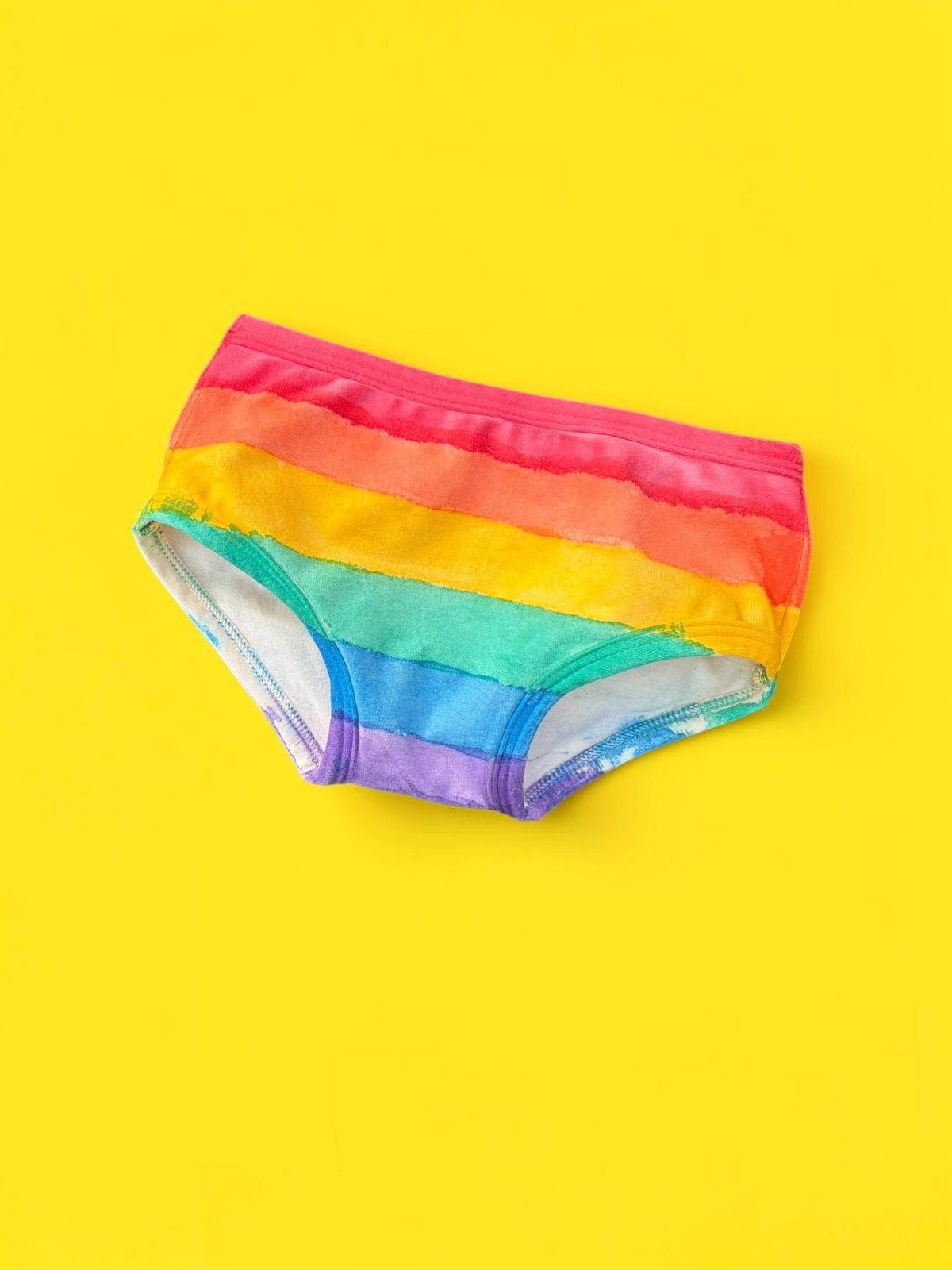 Rainbow-striped kids briefs laid flat on a bright yellow background.