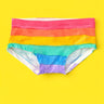 A pair of women's low-rise pants featuring horizontal rainbow stripes in red, orange, yellow, green, blue, and purple, laid flat on a solid bright yellow background.