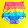 Rainbow-striped high-waisted briefs laid flat on a bright yellow background.