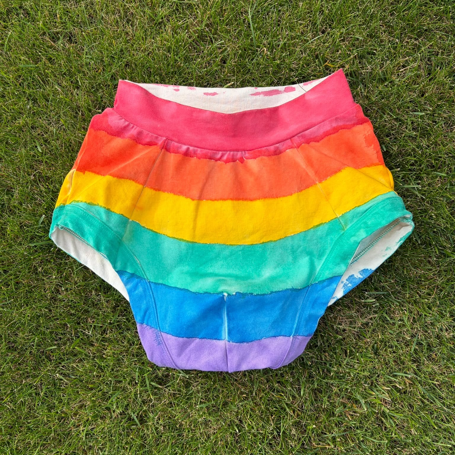 Rainbow-striped briefs bottoms laid flat on green grass.