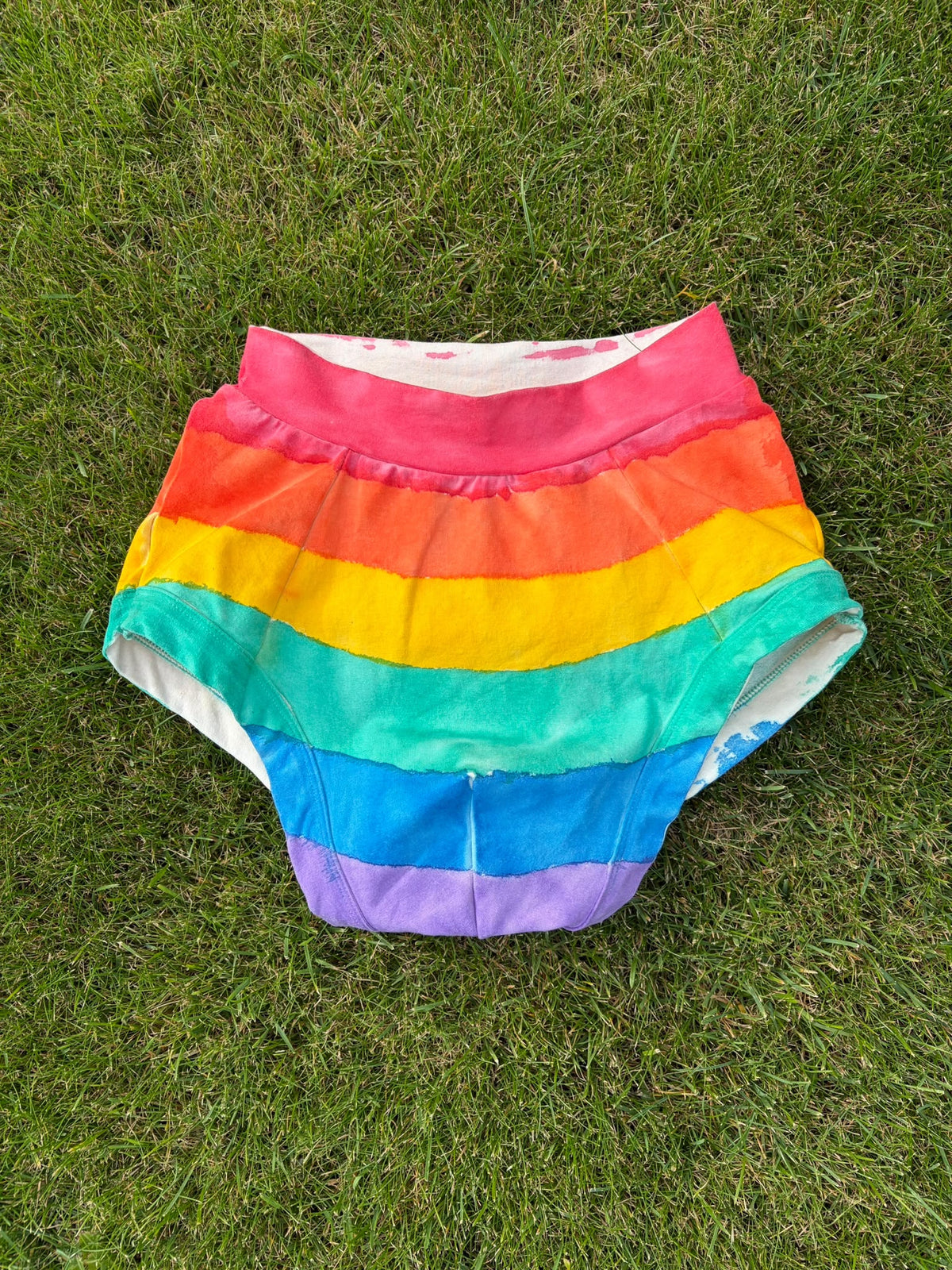 Rainbow-striped briefs bottoms laid flat on green grass.