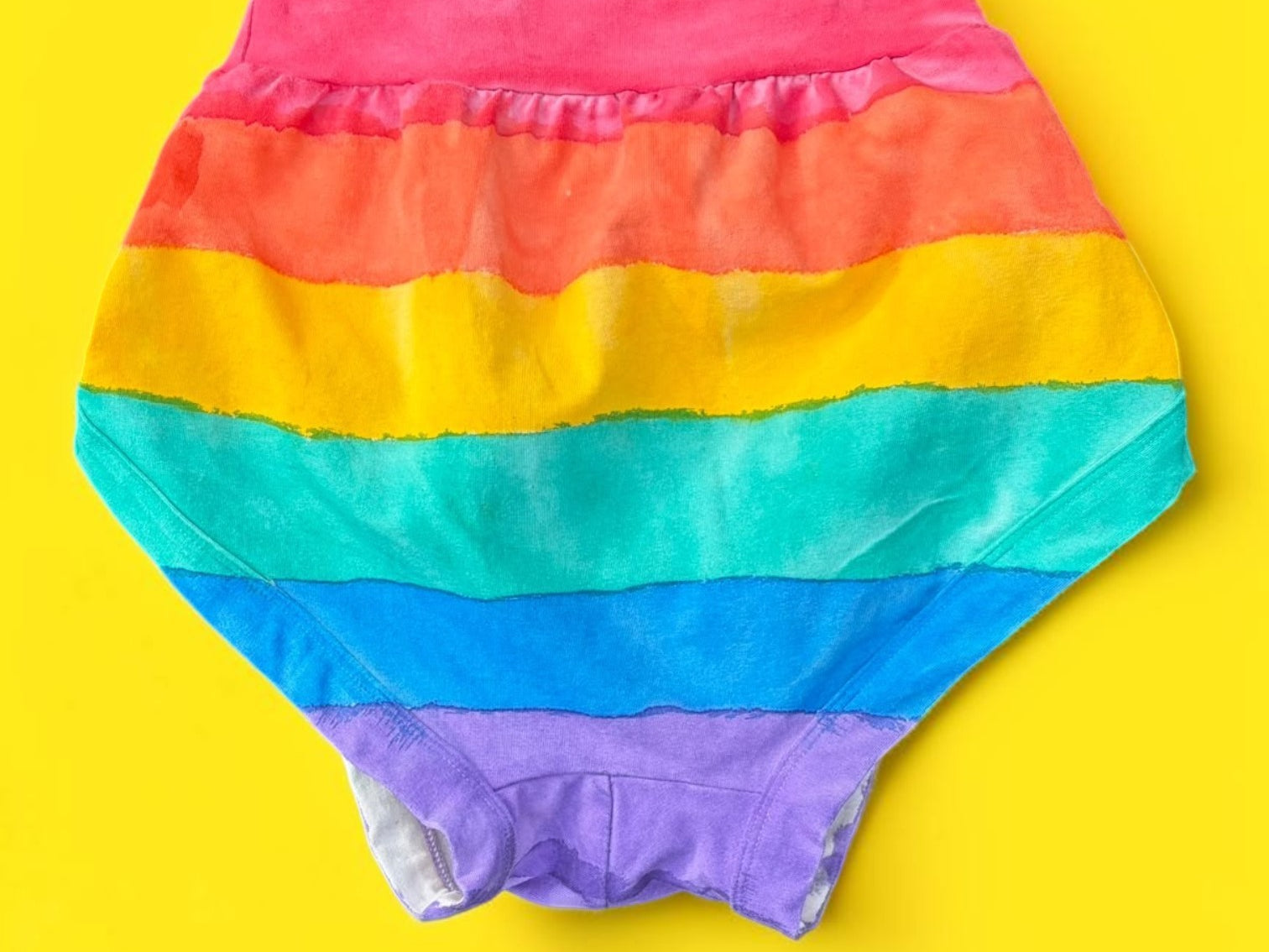 Rainbow-striped Thunderpant briefs back laid flat on a bright yellow background.